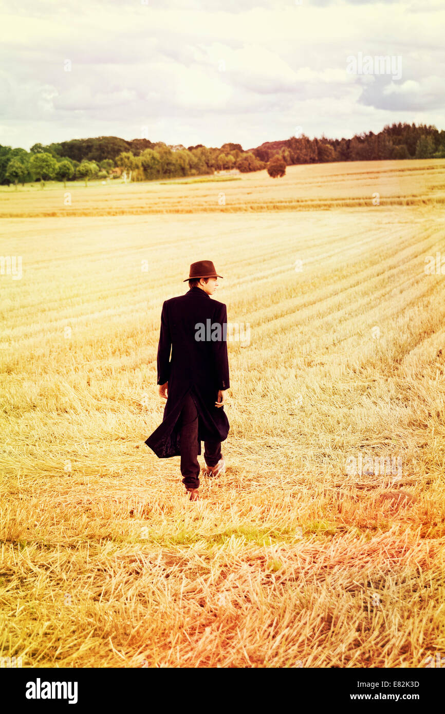 Teenage boy with hat and coat walking on stubble field Stock Photo