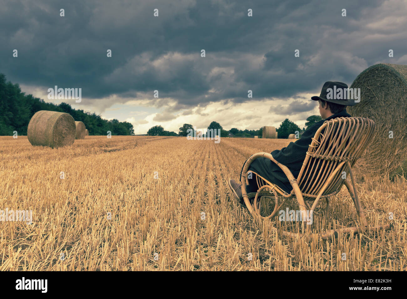 Teenage boy with hat sitting in a rocking chair on a grainfield Stock Photo
