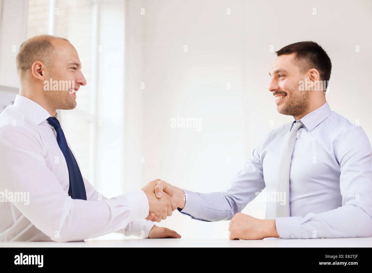 two smiling businessmen shaking hands in office Stock Photo - Alamy