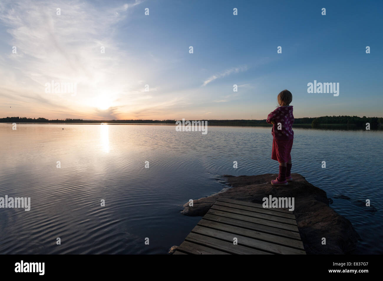 Little child standing by lake shore late summer evening Stock Photo