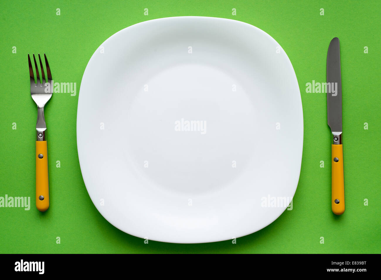 white empty plate with fork and knife on green tablecloth Stock Photo
