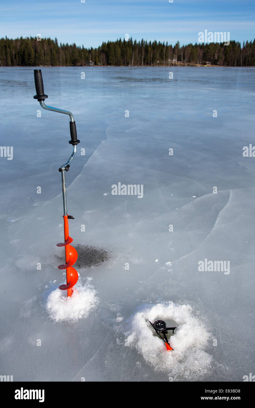Isolated hand ice auger and tip-up ice fishing rod at frozen lake