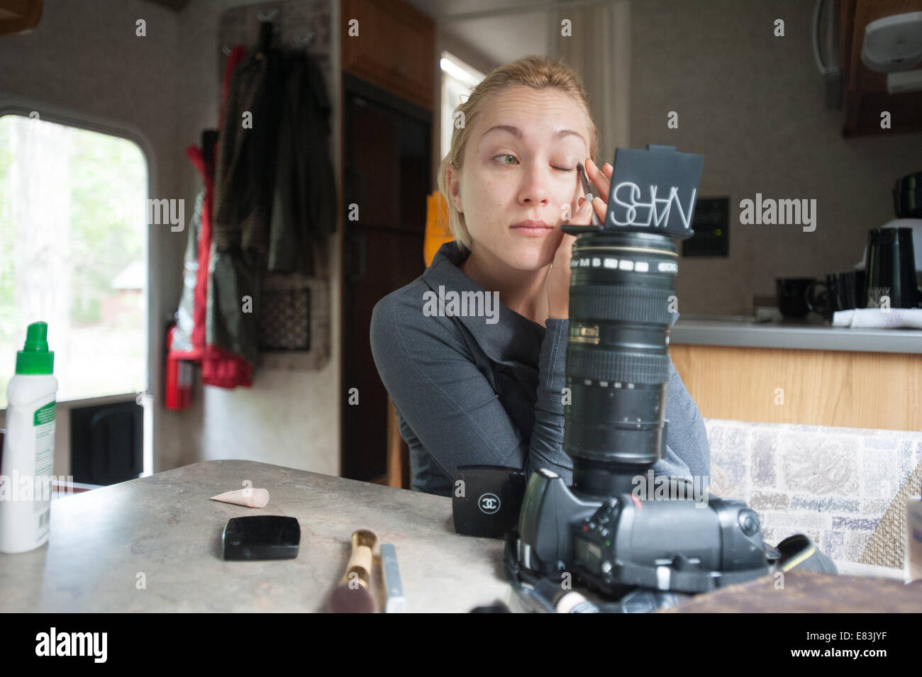 Model applies makeup in RV using camera as mirror stand Stock Photo