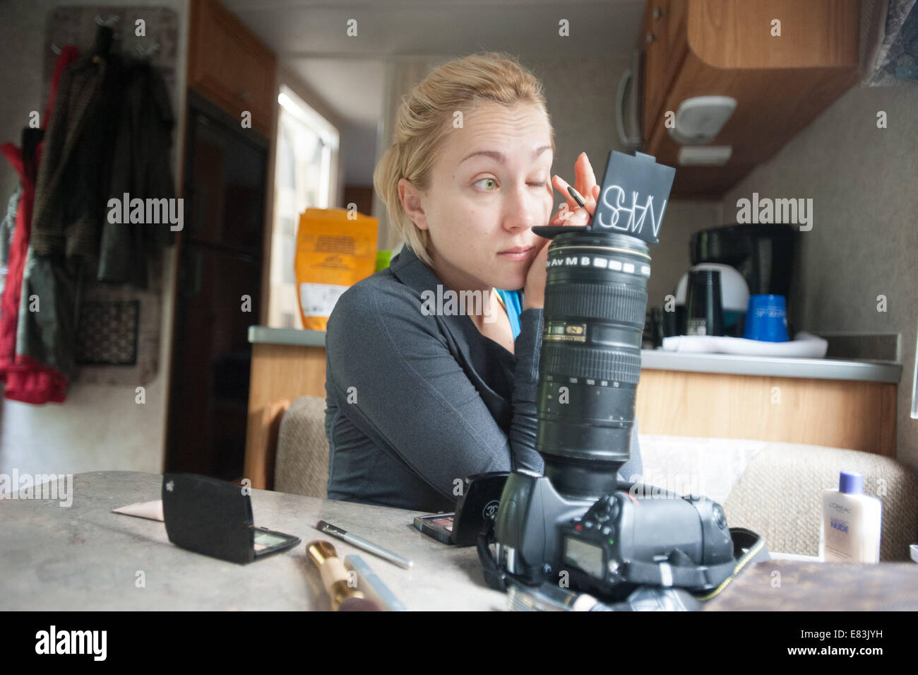 Model applies makeup in RV using camera as mirror stand Stock Photo