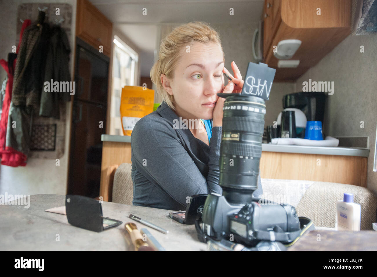Model applies makeup in RV using camera as mirror stand Stock Photo