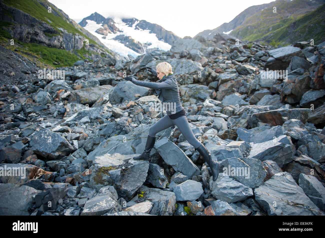 Woman scrambling over rocks  by Byron Glacier Alaska Stock Photo