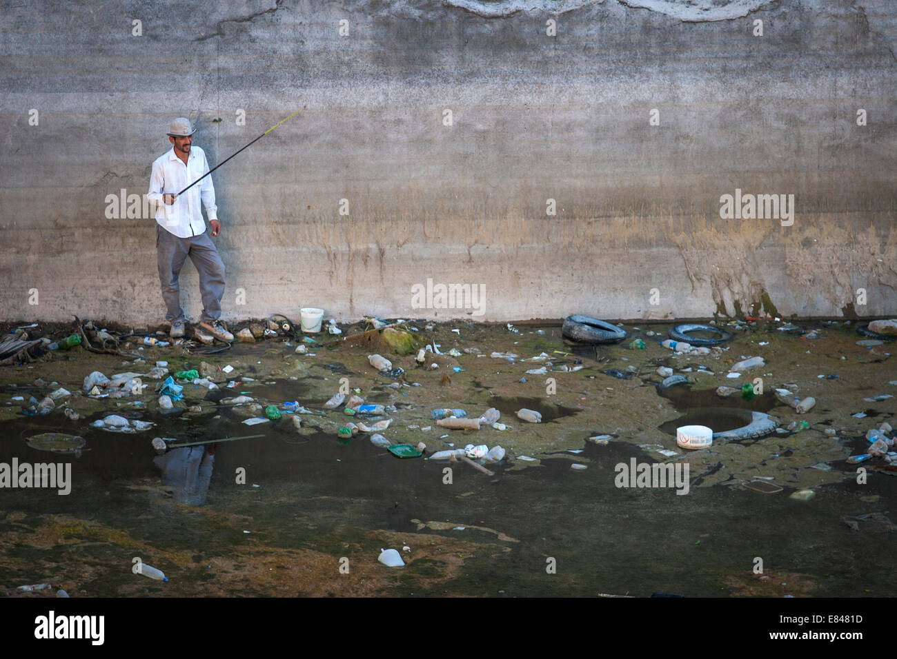 Man fishing in the polluted basin full of plastic waste at the Stock