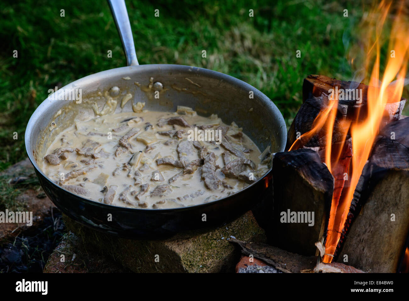 Beef Stroganoff cooked over an open fire outdoors.  This type of fire is known as a Finnish Stove, Swedish Candle or Rocket Fire Stock Photo