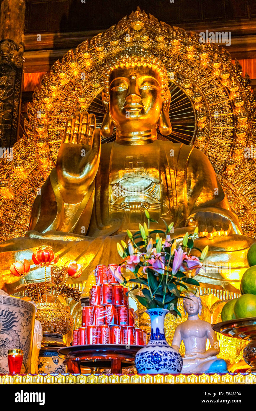 Chua Bai Dinh Buddhist Pagoda: Pile of red Coca Cola cans in front of giant golden Buddha. Stock Photo