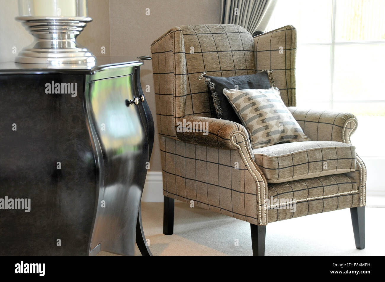 An easy chair and two cushions near a window in a lounge, with sideboard Stock Photo