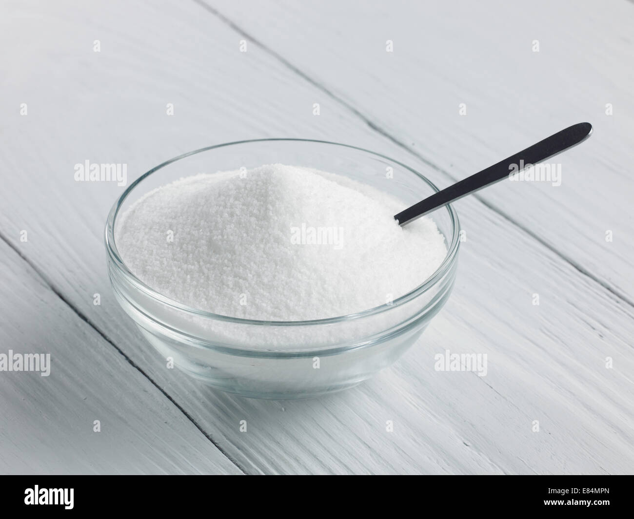 a glass bowl of granulated sugar with spoon on a wooden background Stock Photo