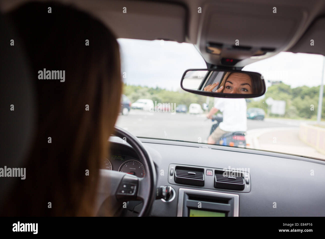 Young, woman driving a car, going home from work, fixing her makeup