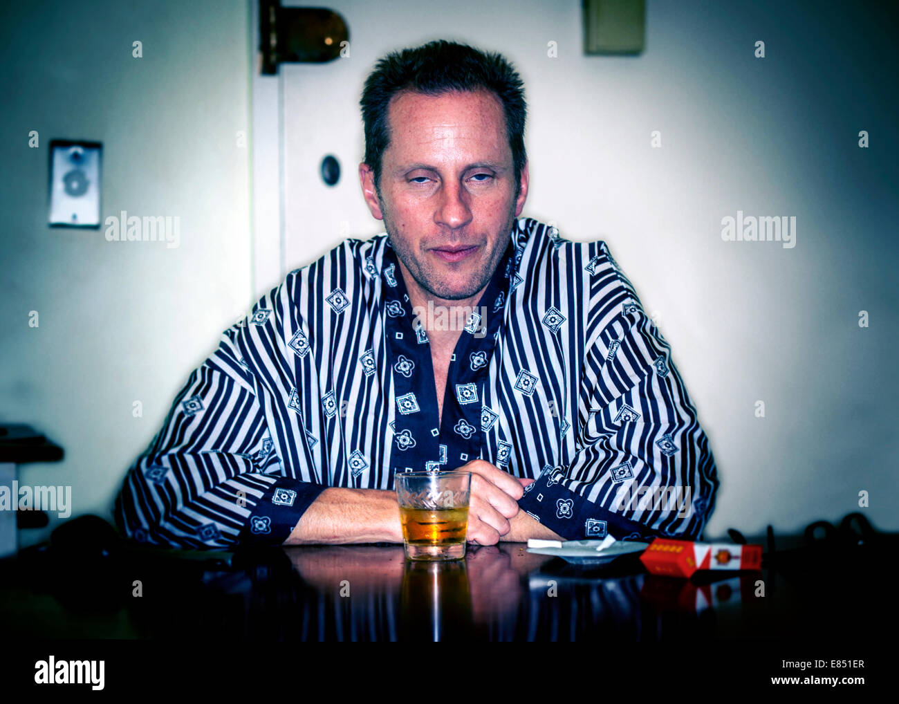 Man sitting in silky robe with whiskey and cigarettes Stock Photo