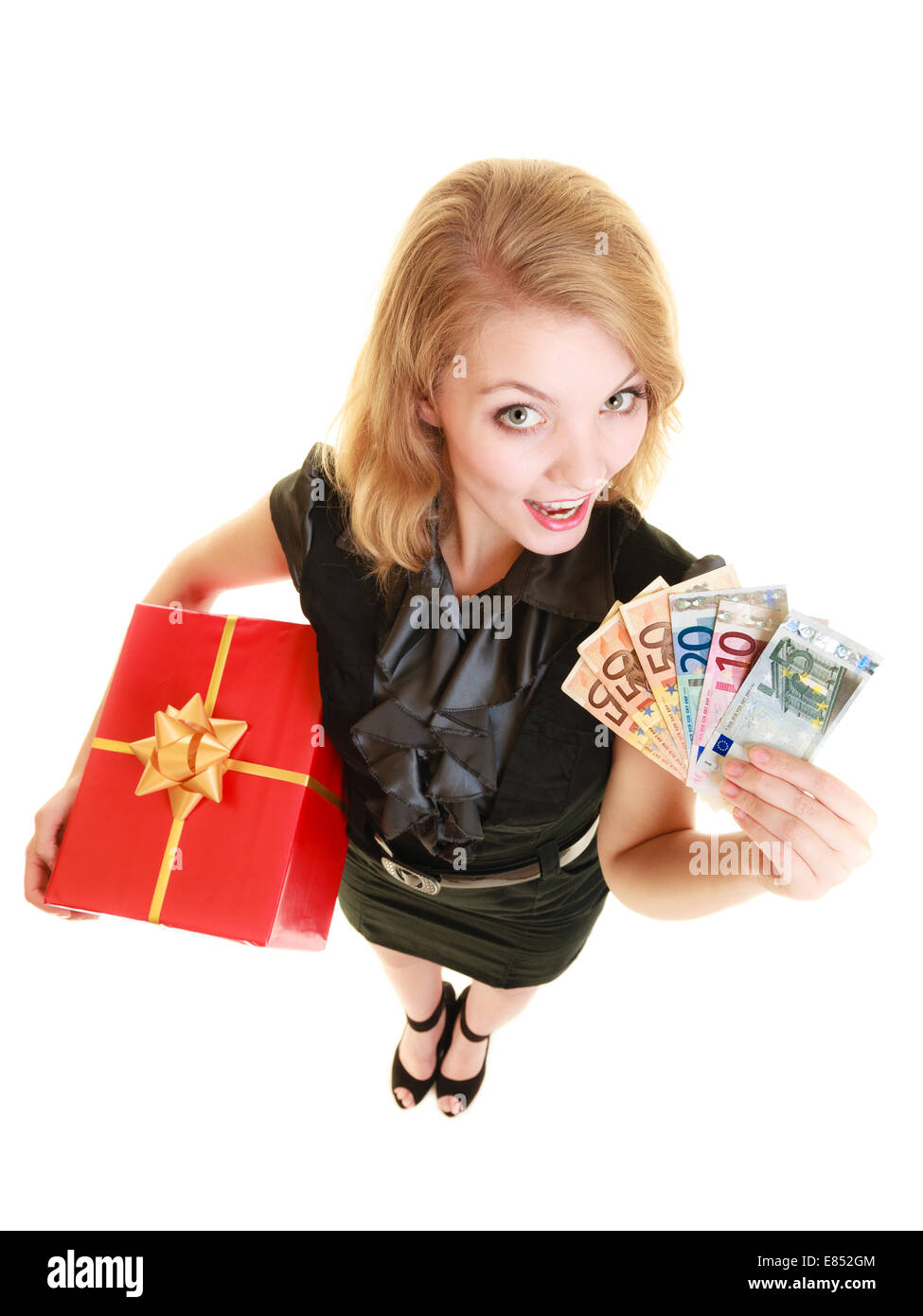 Happy smiling blonde girl young woman holding red christmas gift box and euro currency money banknotes. Holidays time for gifts. Stock Photo