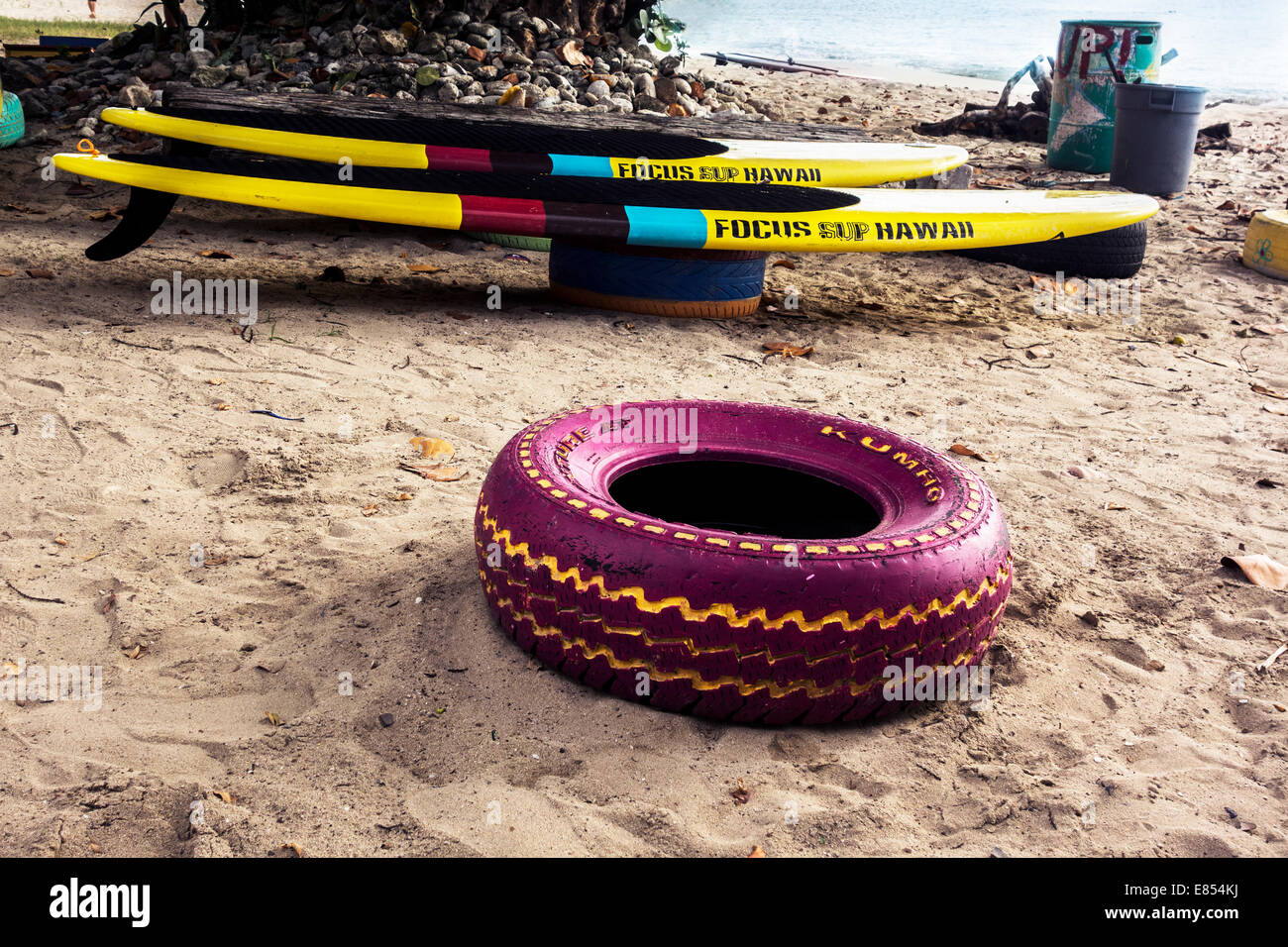 Two stand up paddle boards rest on painted tires, while an empty colorful tire in foreground, near the Caribbean sea. St. Croix. Stock Photo