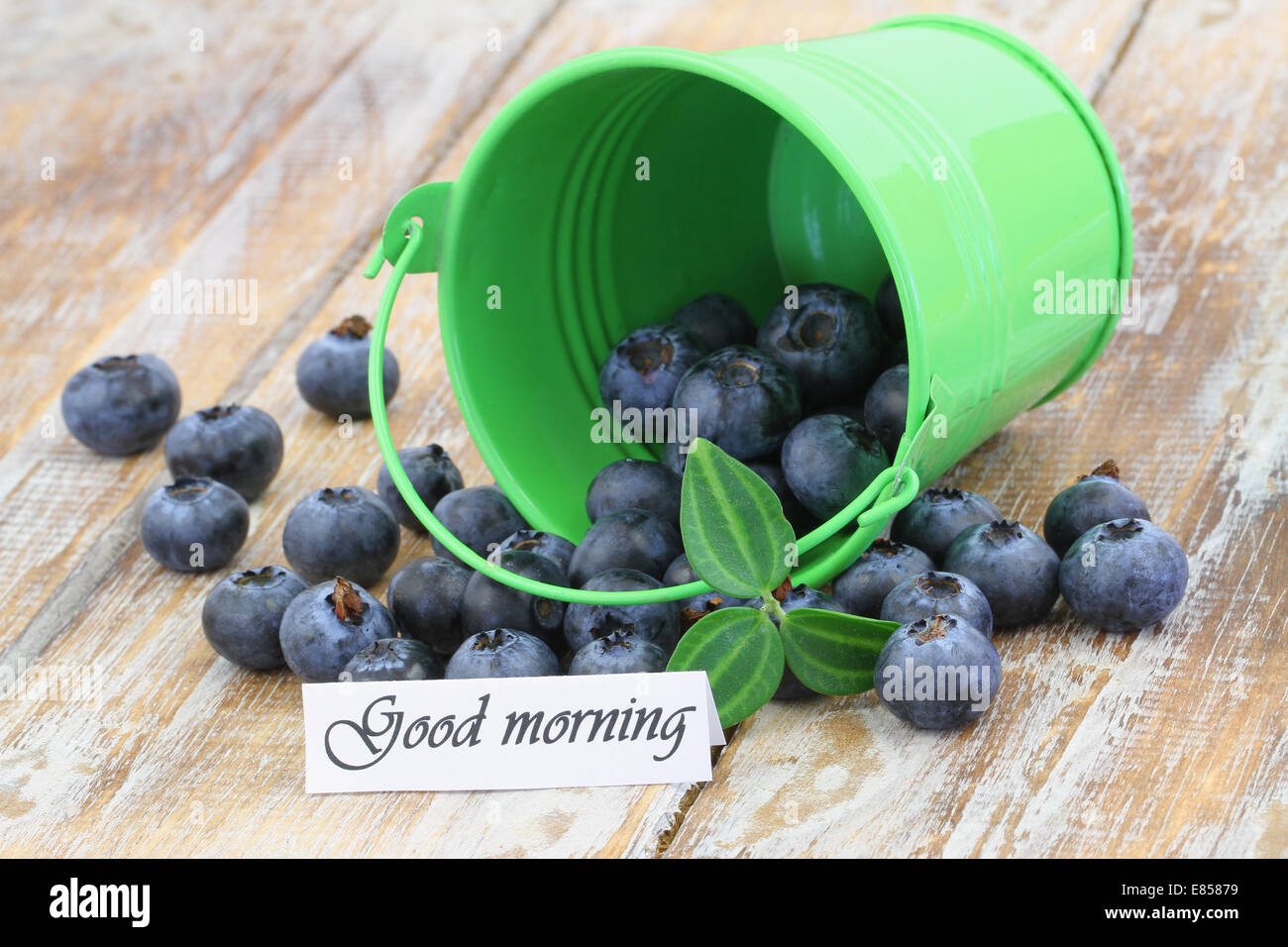 Good morning card with blueberries scattered out of green bucket Stock Photo