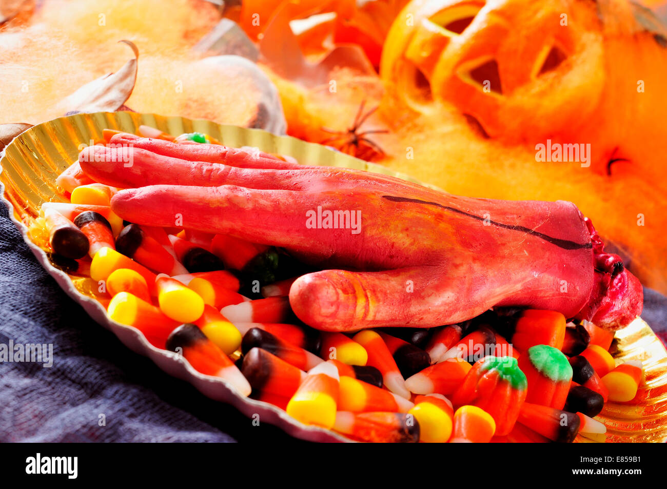 and amputated hand and a pile of Halloween candies with scary ornaments in the background, such as spiders, spider webs and pump Stock Photo