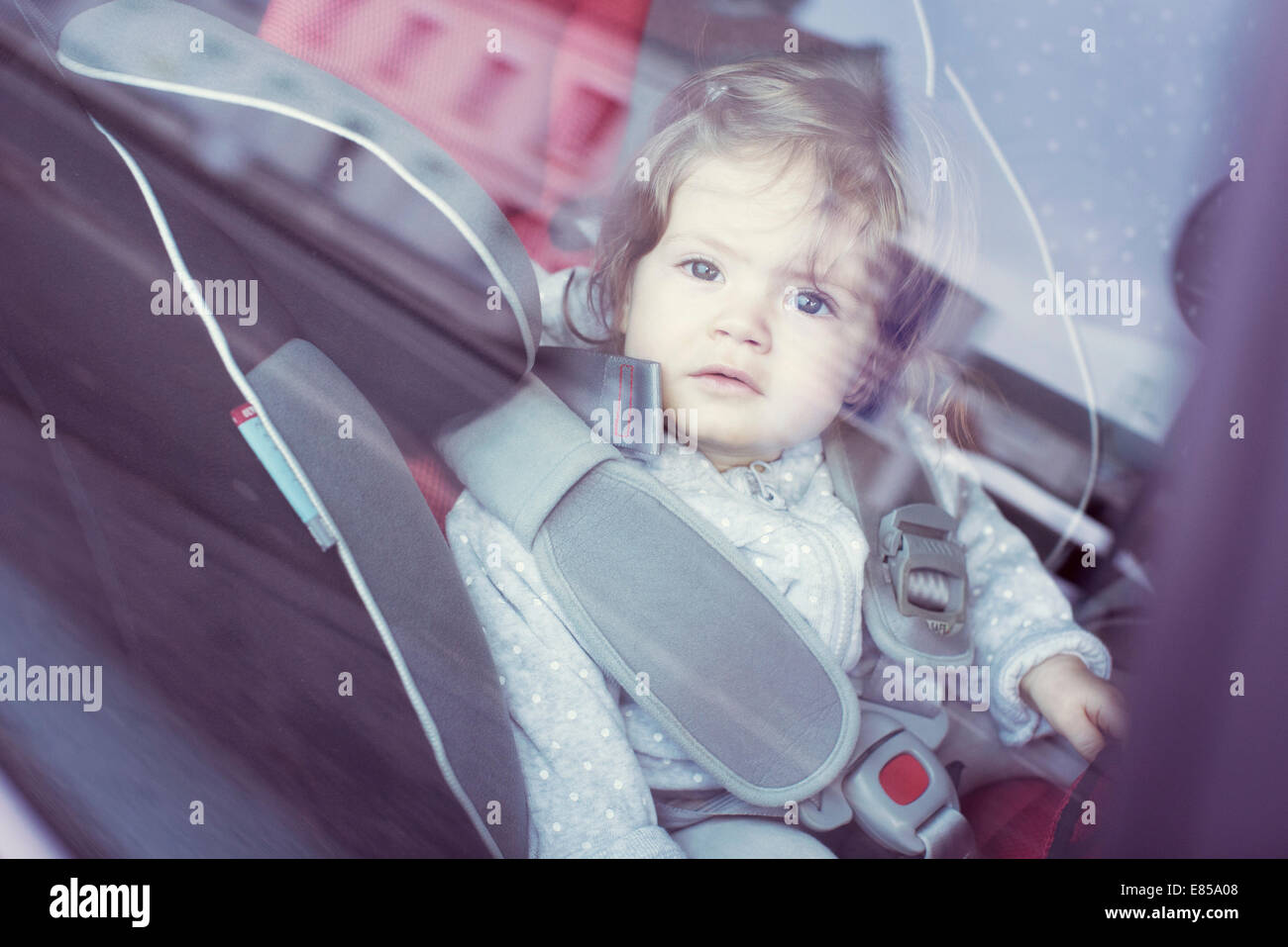 Baby girl sitting in car seat, gazing through car window Stock Photo