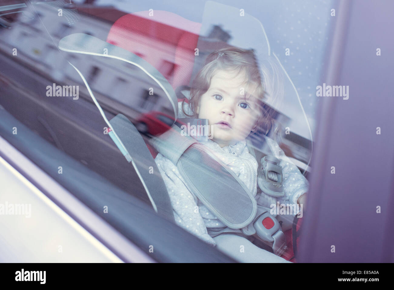 Baby girl sitting in car seat, gazing through car window Stock Photo