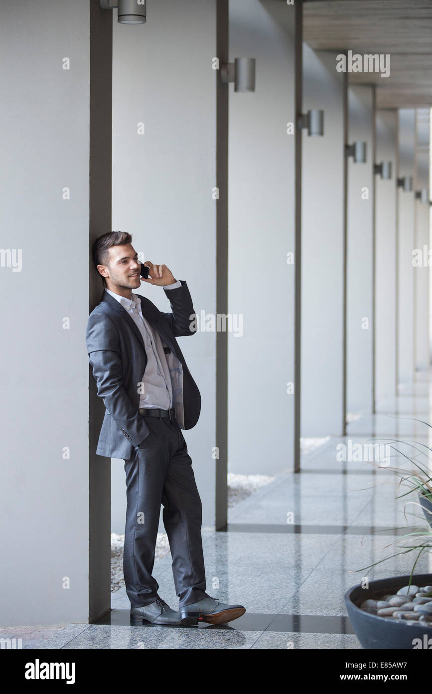 Young executive taking phone call while leaning against column in building lobby Stock Photo