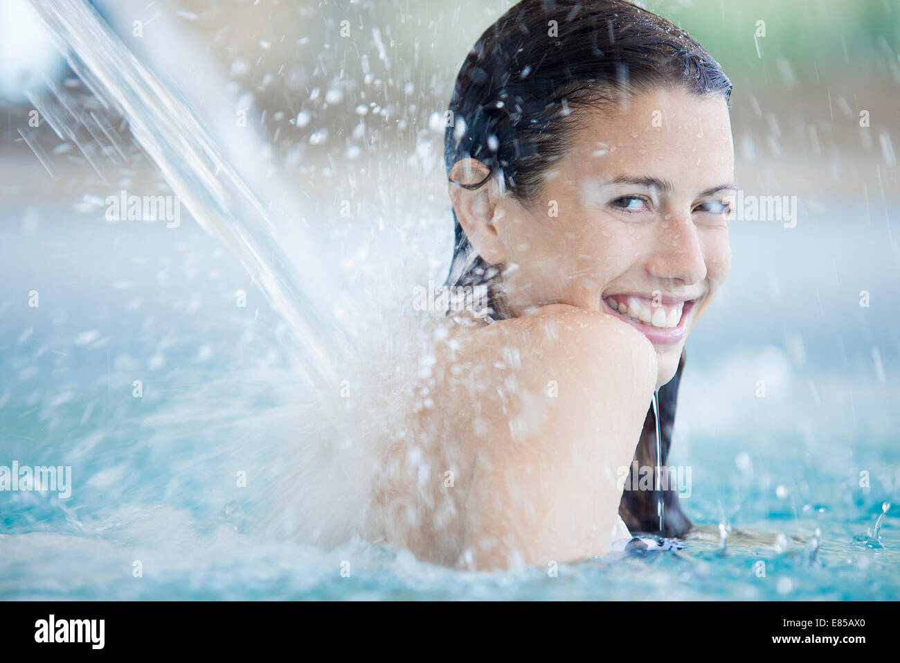 Woman relaxing under fountain in swimming pool Stock Photo