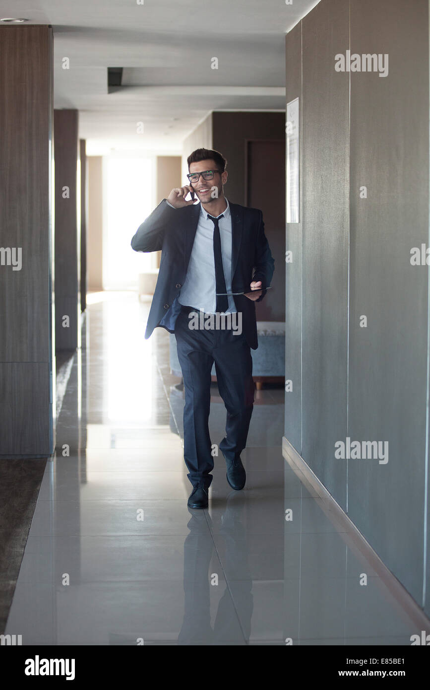 Young businessman talking on phone while walking through office Stock Photo