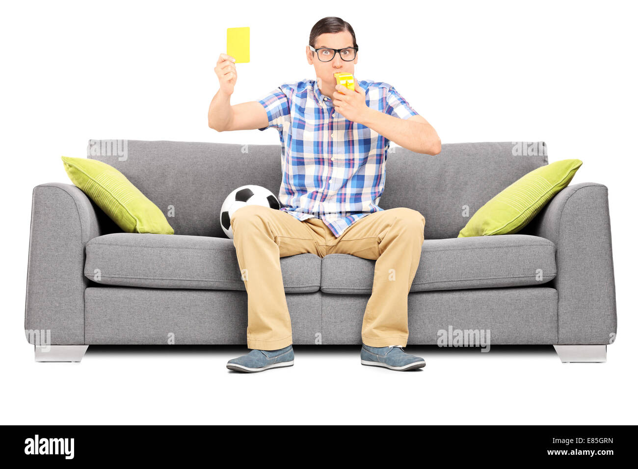 Angry football fan holding a yellow card seated on couch isolated on