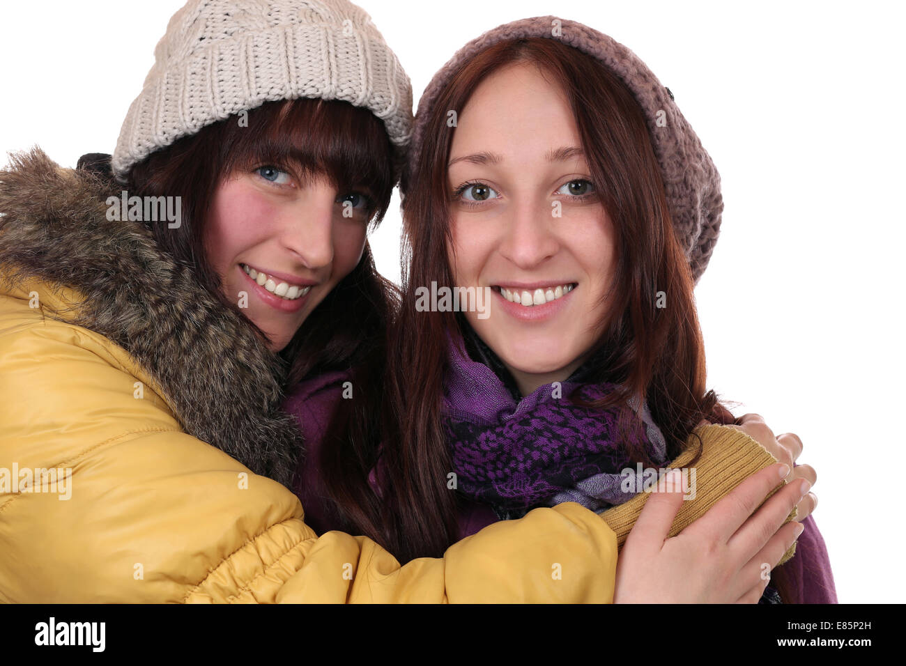 Two smiling women in winter clothing hug each other, isolated on a white background Stock Photo