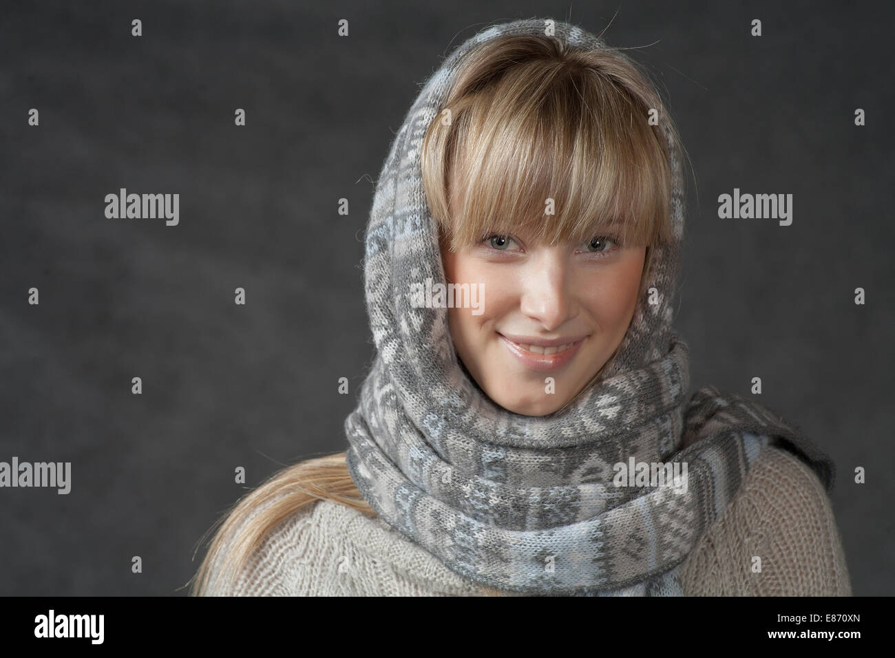 Smiling blonde in studio front view. Portrait of woman on dark background wearing woolen accessories Stock Photo