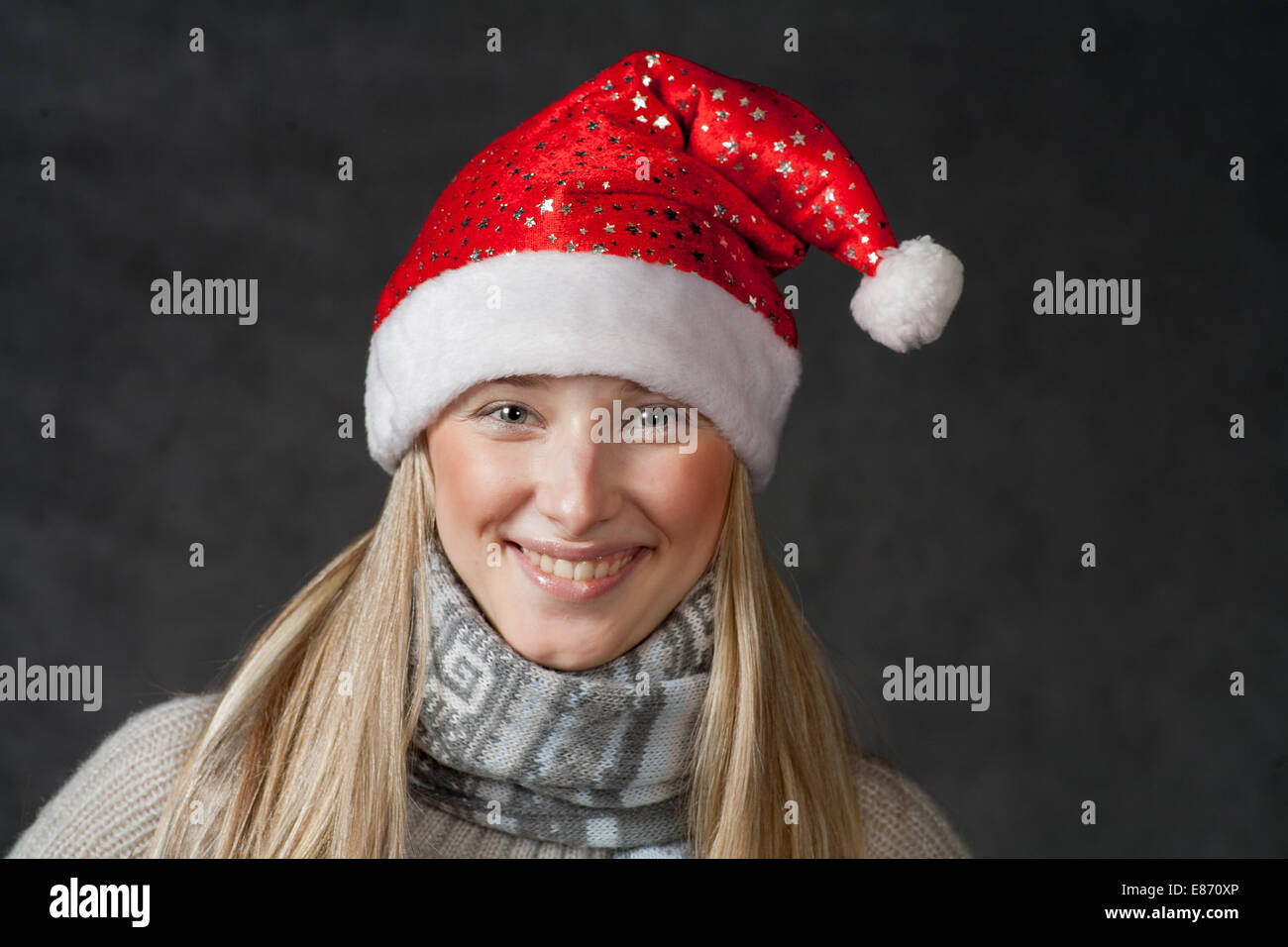 Front view of the smiling blond female in Santa hat. Pretty blond wearing christmas hat on dark background Stock Photo