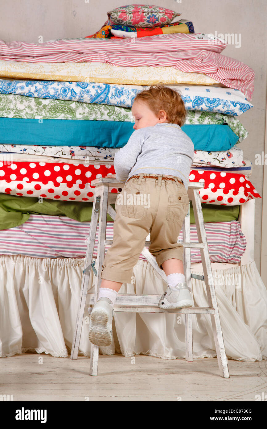 Child climbs on the bed with lots of quilts - Princess and the Pea. Stock Photo