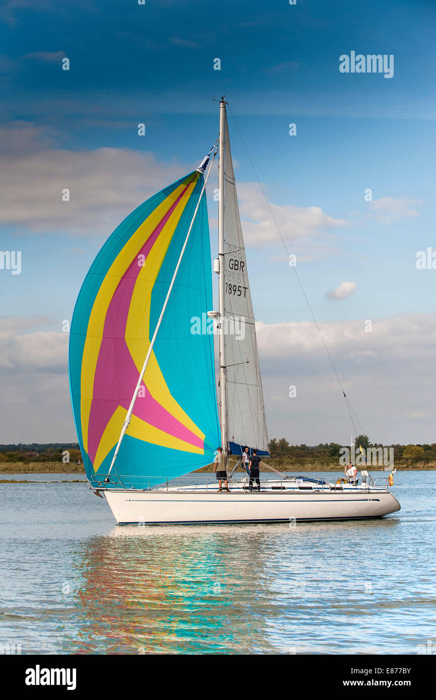 A sailboat using a colourful spinnaker as she sails up the Blackwater River in Essex. Stock Photo