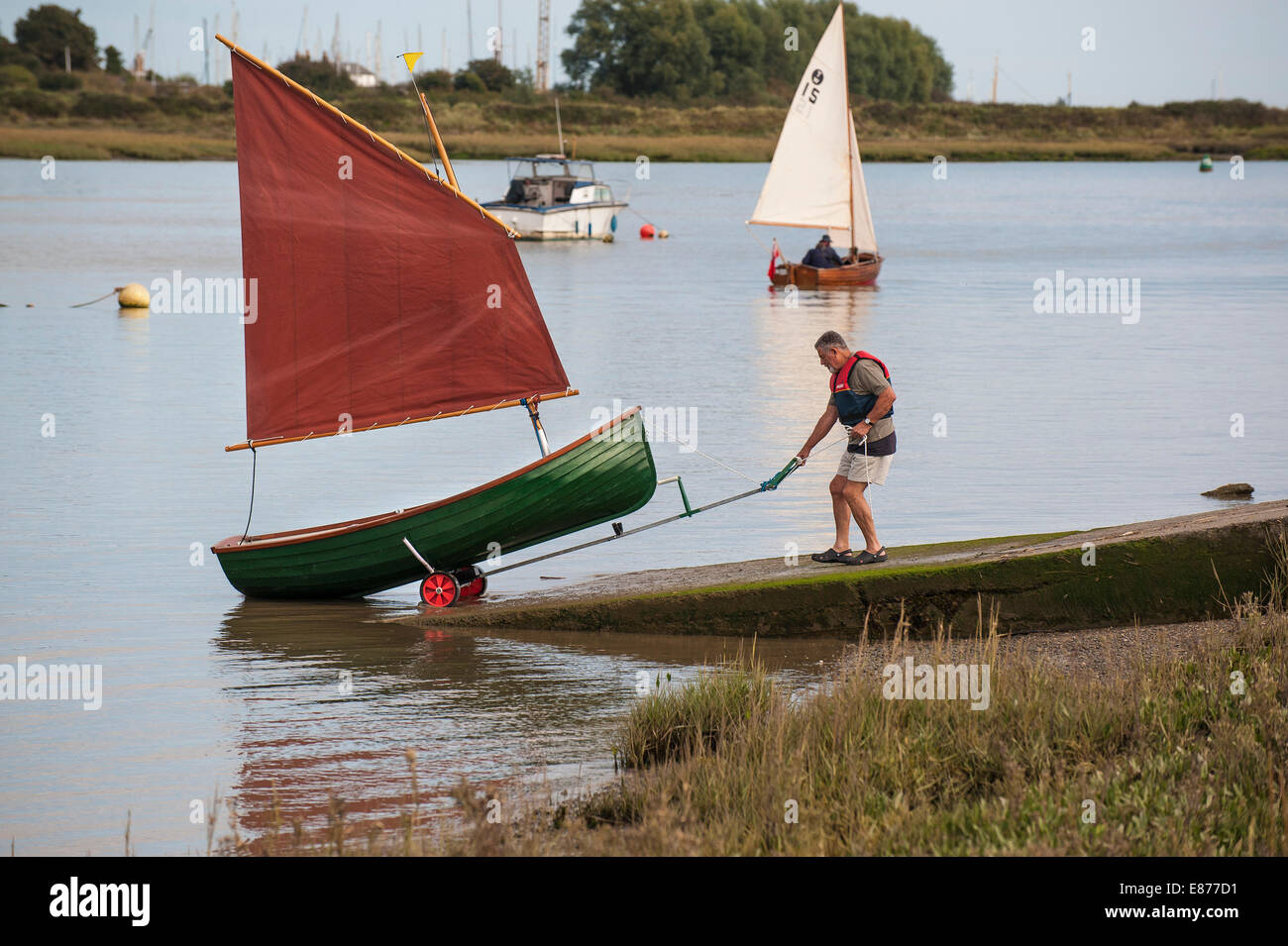 A man launching a Heybridge Roach dinghy on the Blackwater River in Essex. Stock Photo