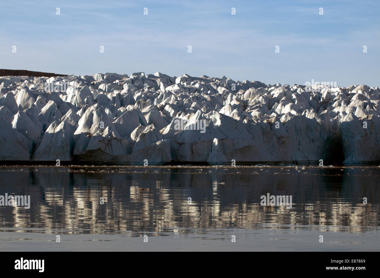 Arctic ice, a glacier pinnacled into a solid, meringue-like wall, is reflected dramatically by evening sunlight Stock Photo