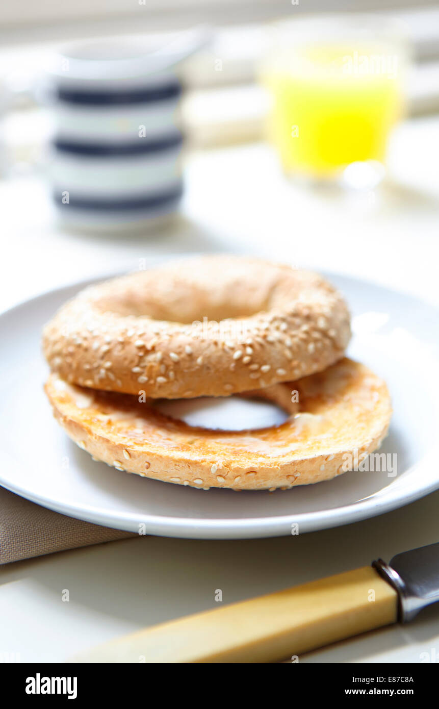 buttered sliced bagel with orange juice in glass jug and Knife Stock Photo