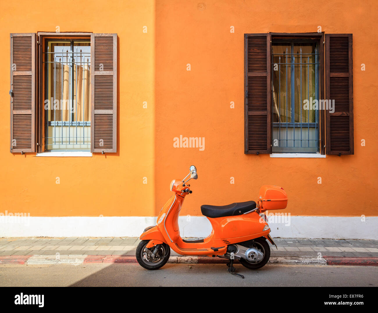 Scooter parked by the curb against orange building in Tel Aviv, Israel Stock Photo