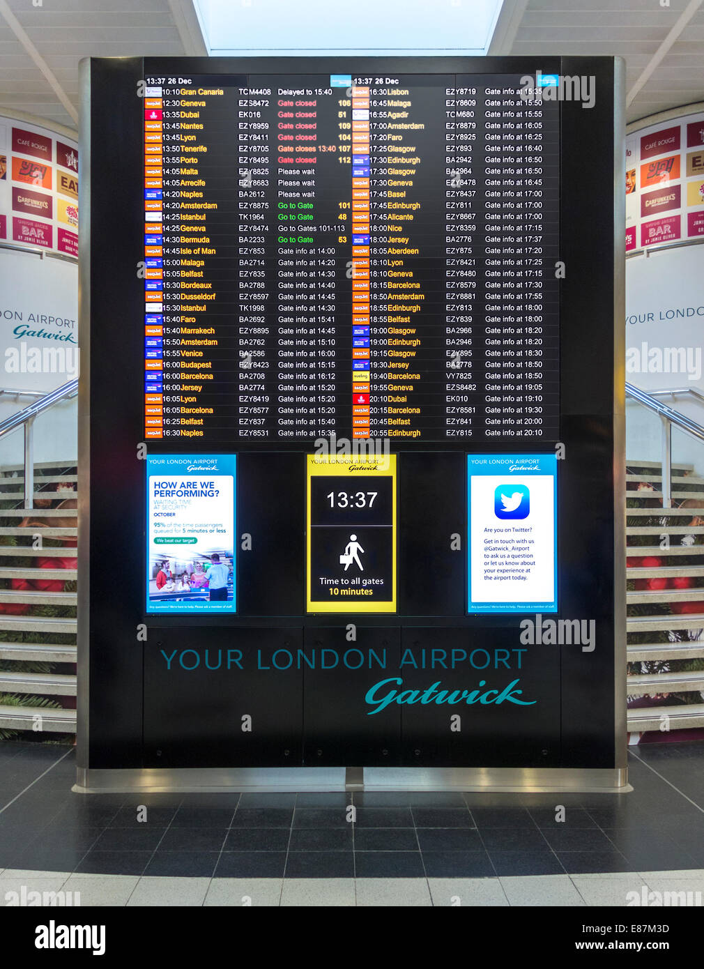 London Gatwick North Terminal gates info and flight departures board. Walking distances sign, clock, Twitter announcement. Stock Photo