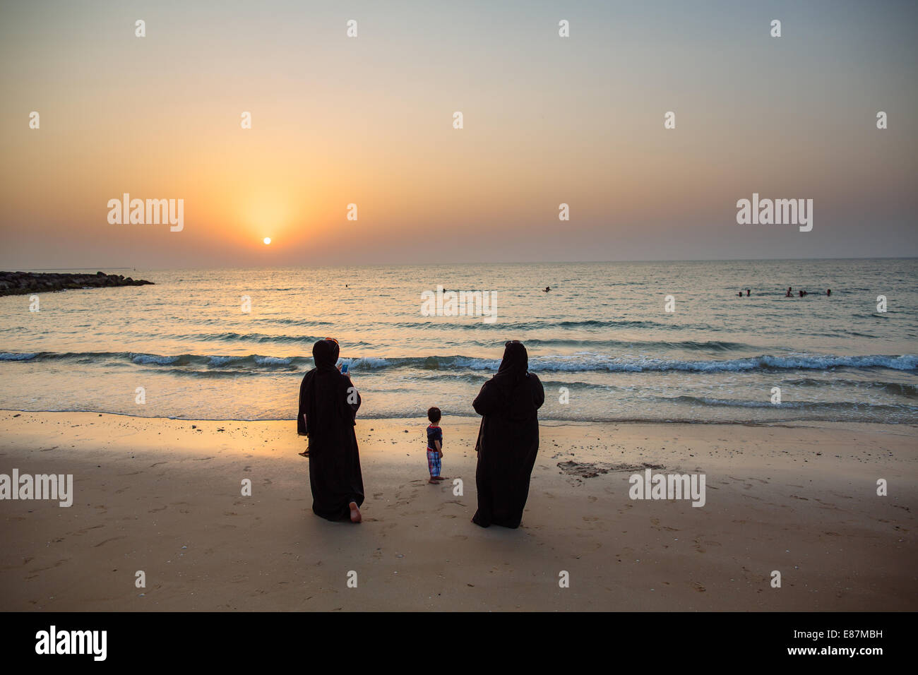 little kid and arab women in traditional clothing with abayah, staring at the sea during sunset, landscape Stock Photo