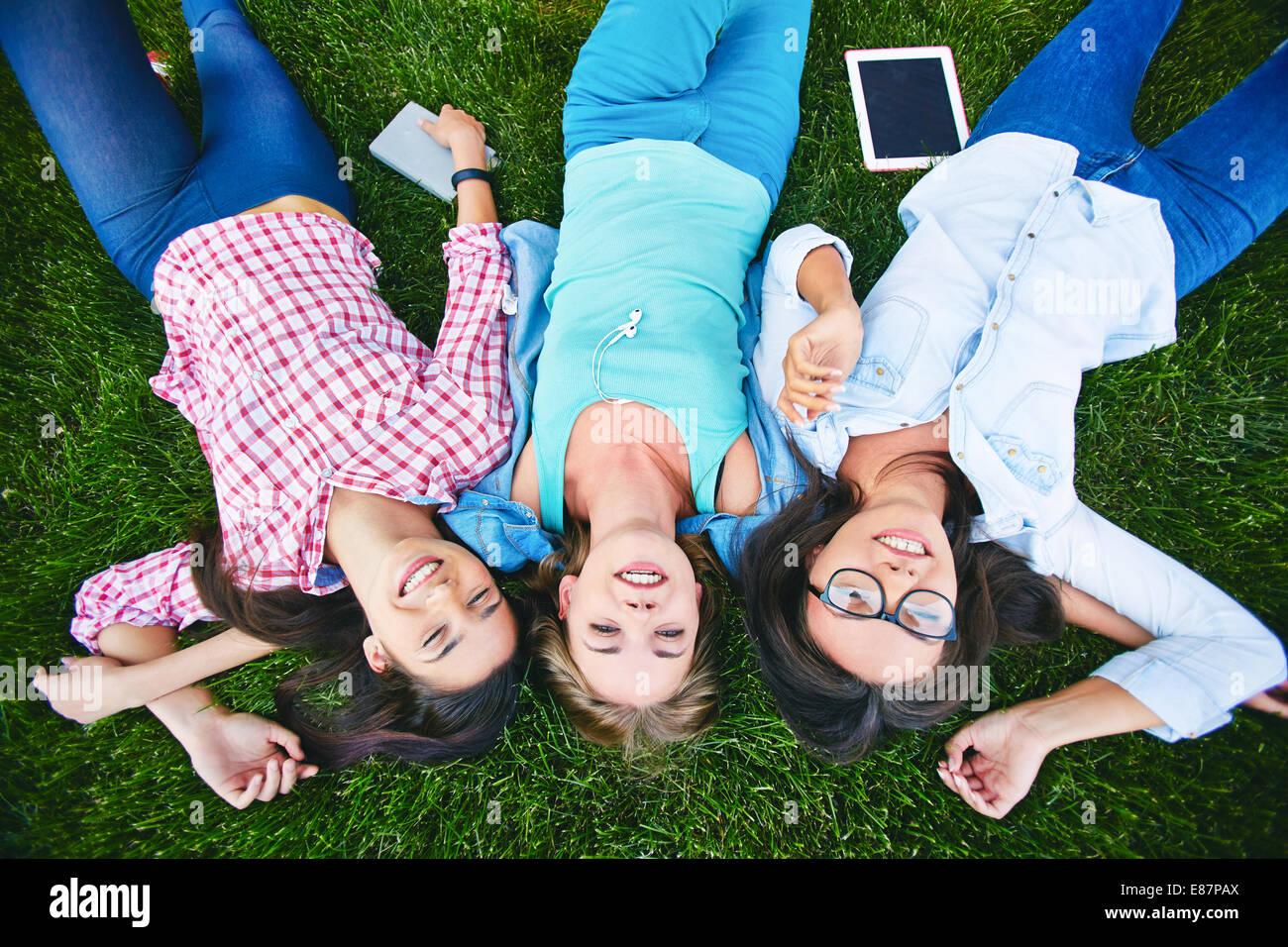 Three cheerful teen girls in casual lying on green grass Stock Photo