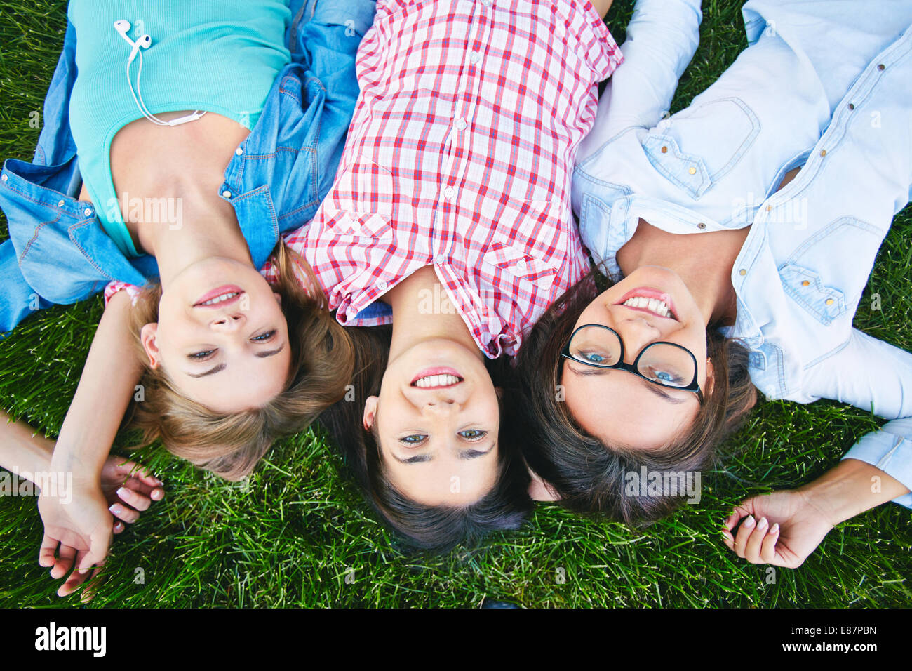 Three cheerful teen girls in casual lying on lawn and looking at camera Stock Photo