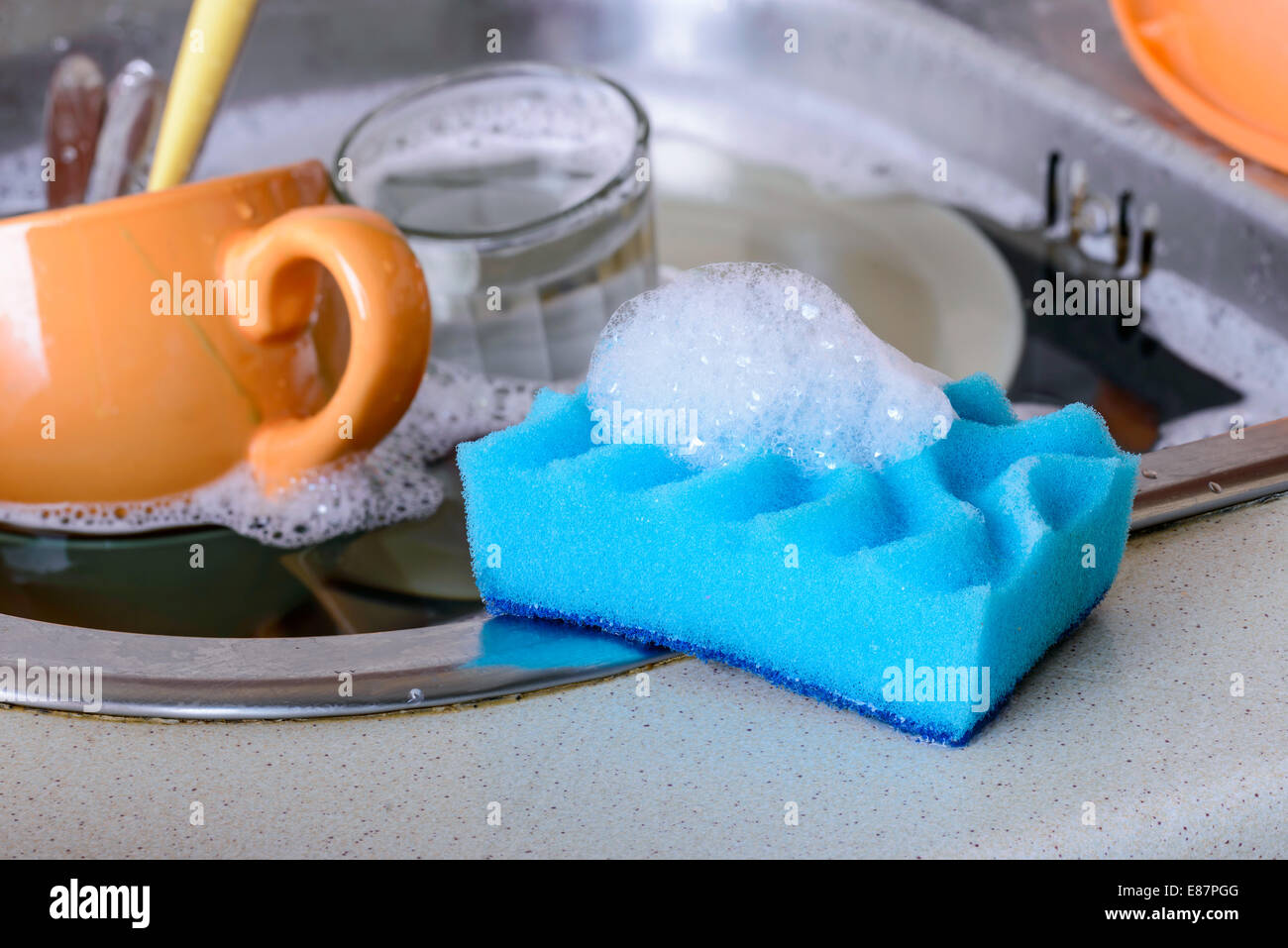 Cleaning the dirty dishes with a blue sponge with detergent in a sink