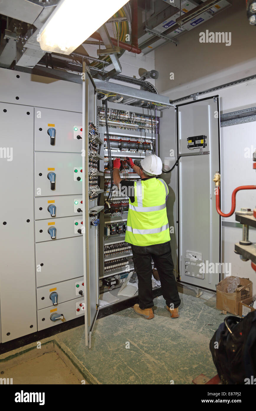 A building services engineer works in an electrical control cabinet in the plant room of a large office block Stock Photo