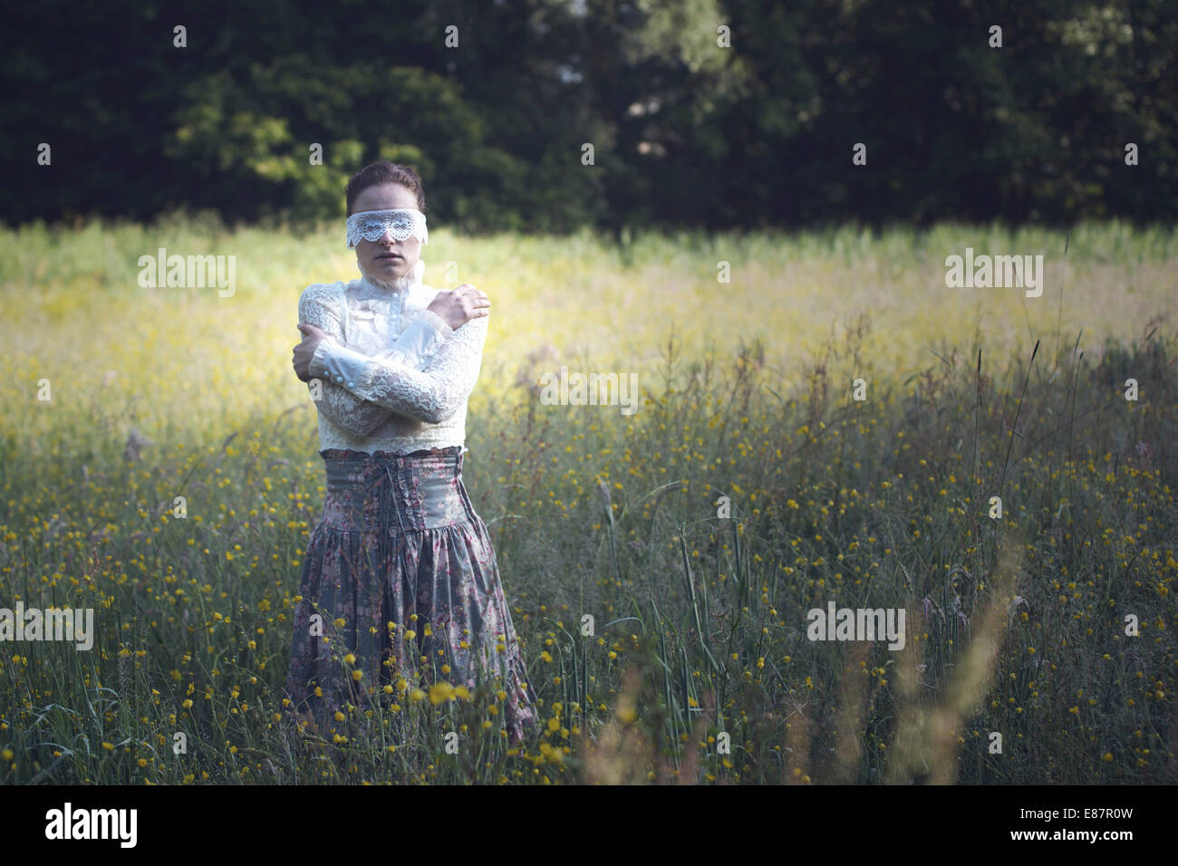 Woman with a lace mask in front of her eyes standing in a meadow Stock ...