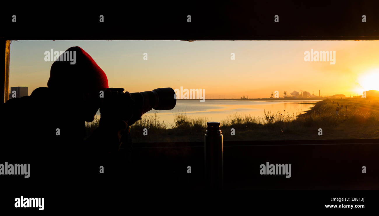 Female photographer in hide at sunrise at Teesmouth National Nature Reserve, Hartlepool, UK. Stock Photo