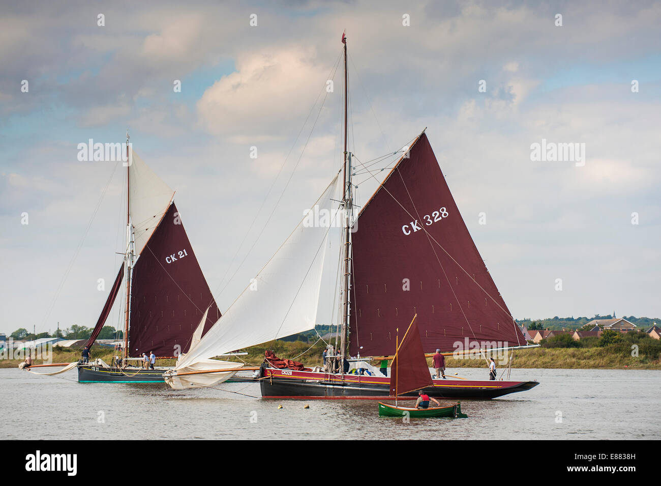East Coast gaff rigged fishing smacks sail past a small Haybridge Roach dinghy during the Parade of Sail at the Maldon Regatta. Stock Photo