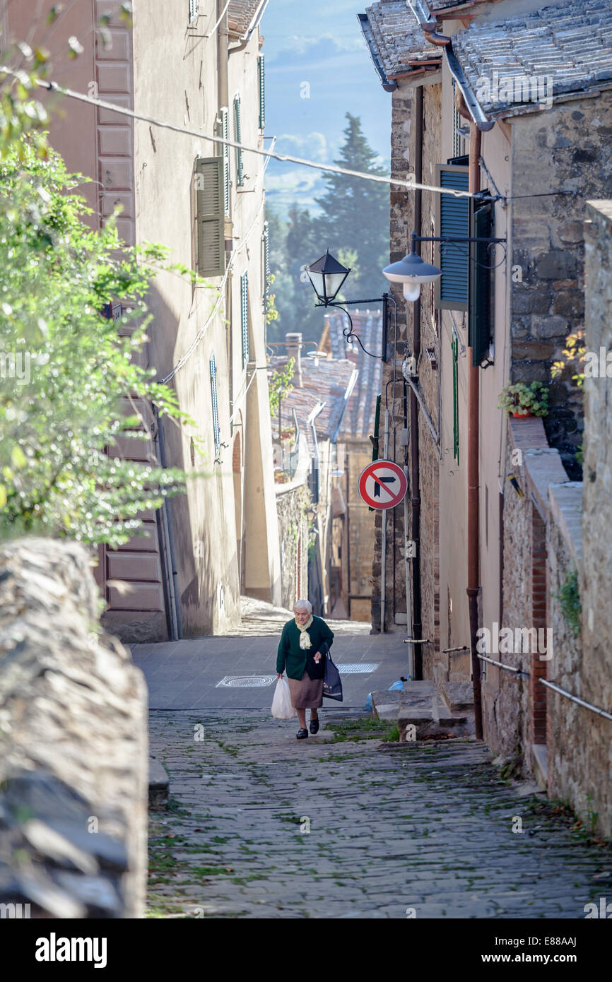 Old sad woman carrying two bags in the narrow street in Montalcino Italy Tuscany Stock Photo