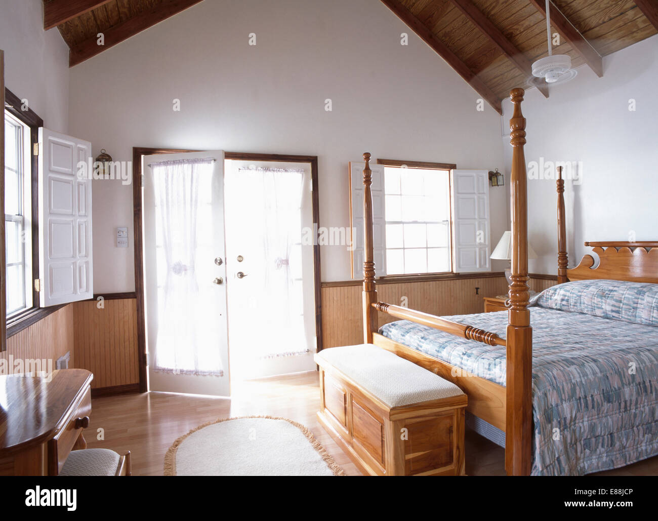 Wooden ottoman below bed with blue patterned quilt in light and airy bedroom Stock Photo