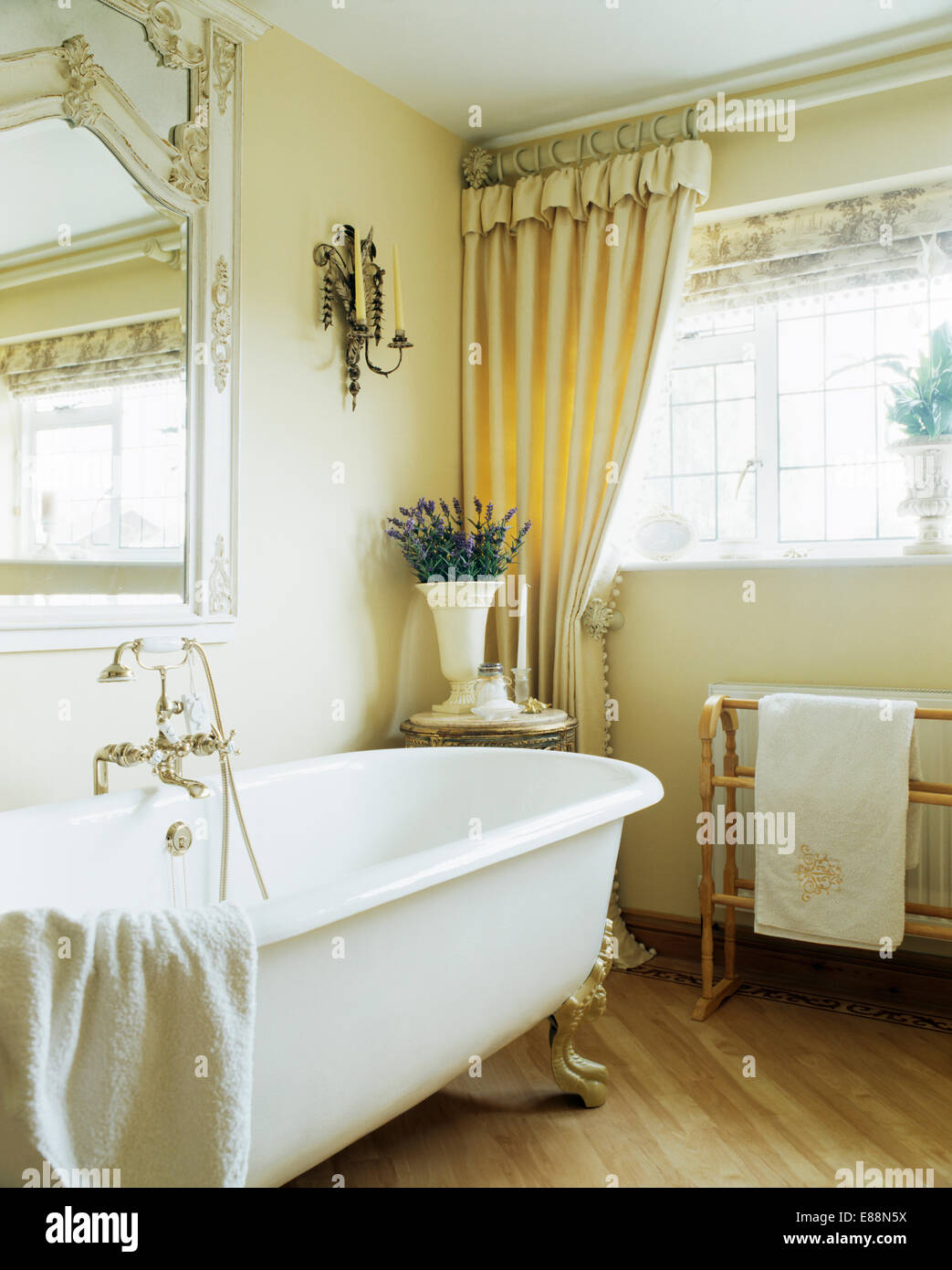 Roll-top bath in cream bathroom with cream curtains on window above heated  towel-rail Stock Photo - Alamy