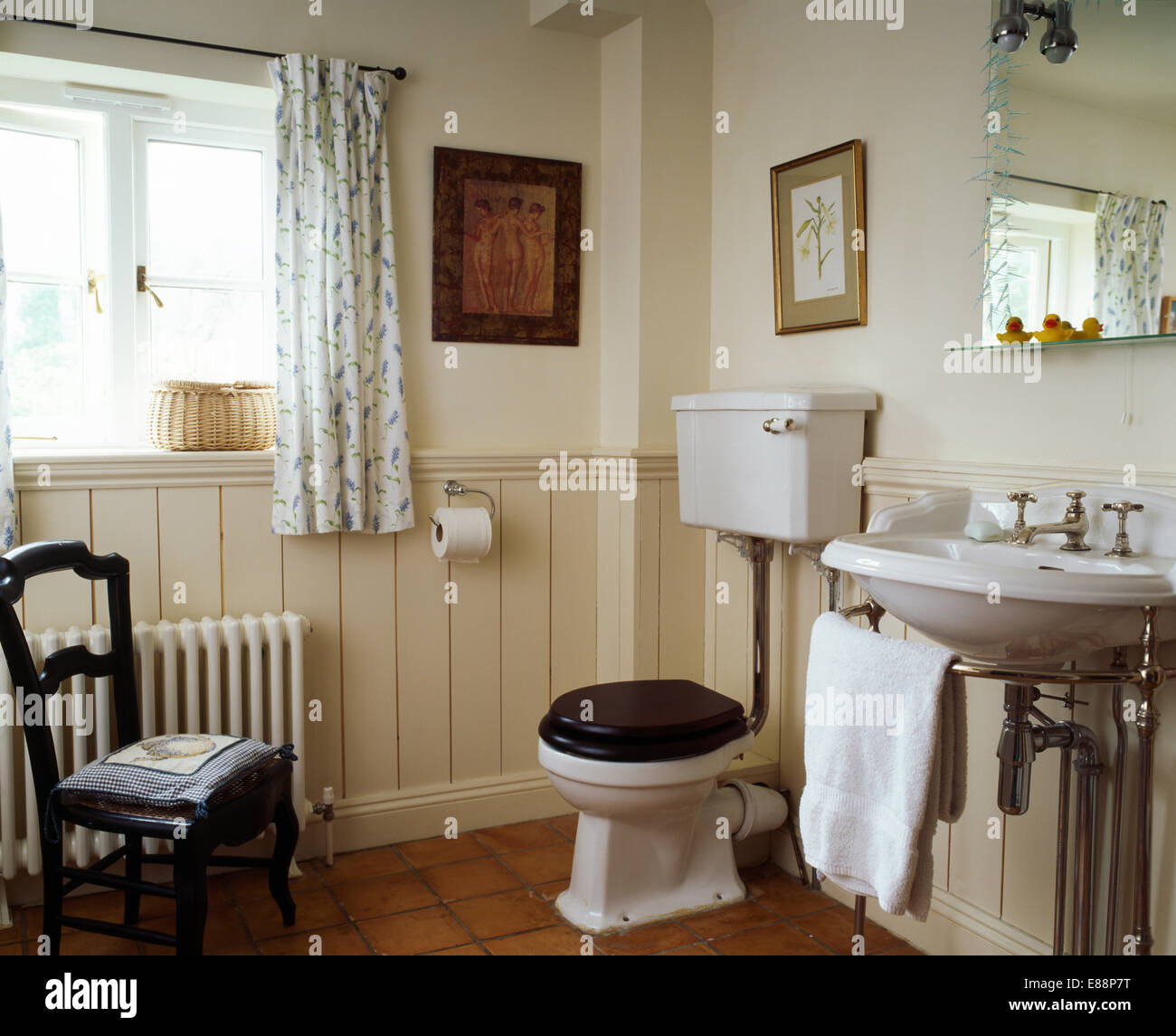 Cream dado tongue+groove panelling in country bathroom with antique chair beside white radiator Stock Photo