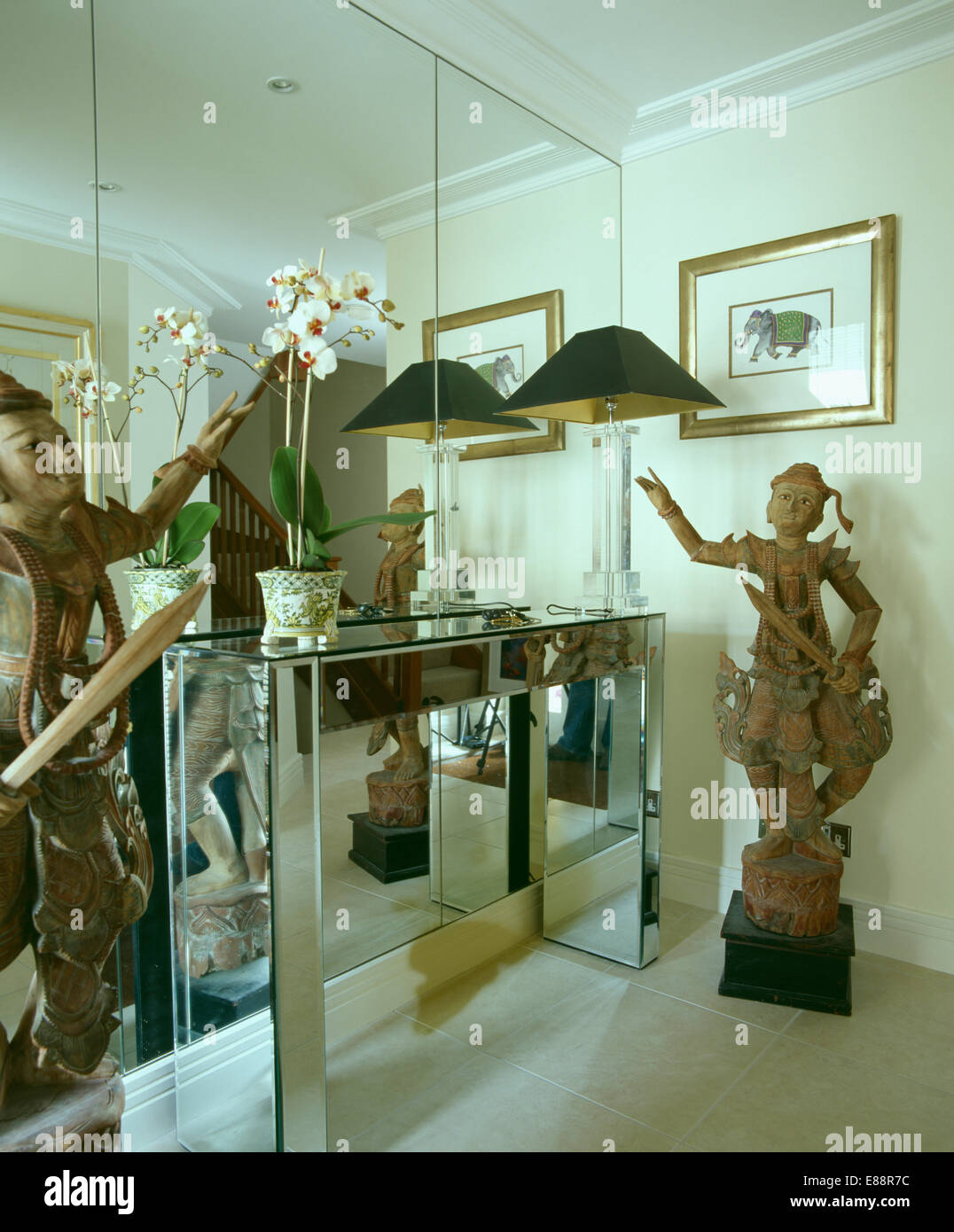 Tall Chinese statue beside mirrored console table against mirrored wall in modern townhouse hall Stock Photo
